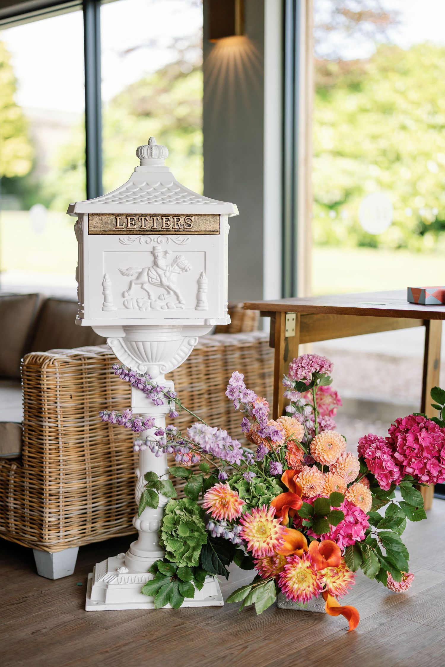 Elegant white decorative urns and wicker baskets arranged with vibrant pink, orange and coral flowers on a wooden table.