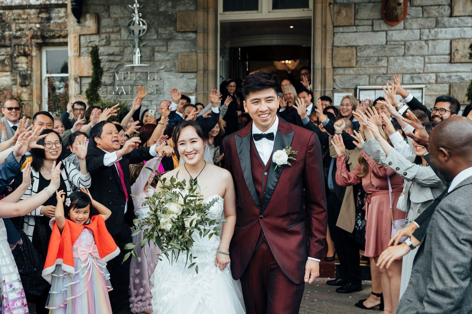 Wedding guests celebrate with raised arms and cheers at a rustic stone venue during a joyful reception moment.