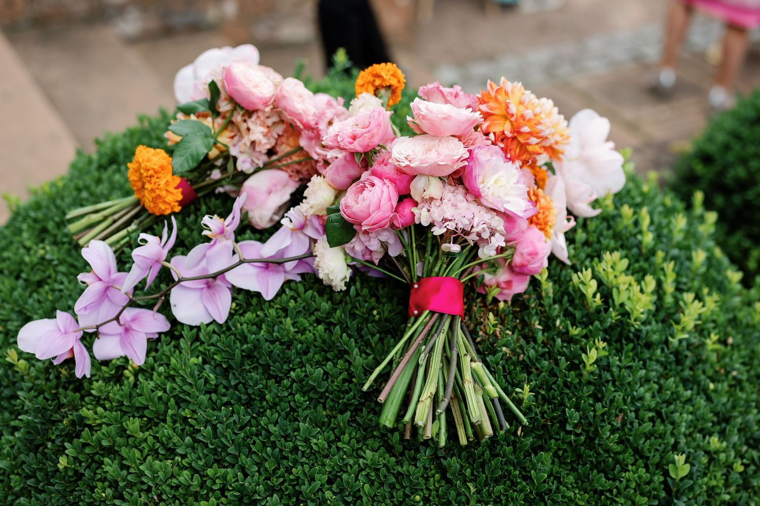 A vibrant floral bouquet with pink and orange blooms rests on a mossy green surface in a garden setting.