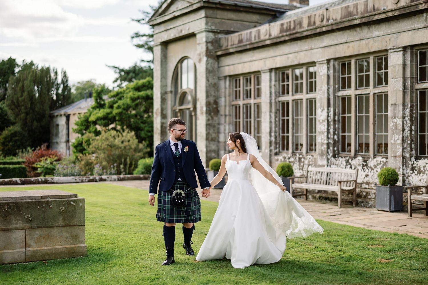 “Bride and groom standing in front of Kinmount House, a stately Scottish mansion with sweeping lawns and classic architecture.”