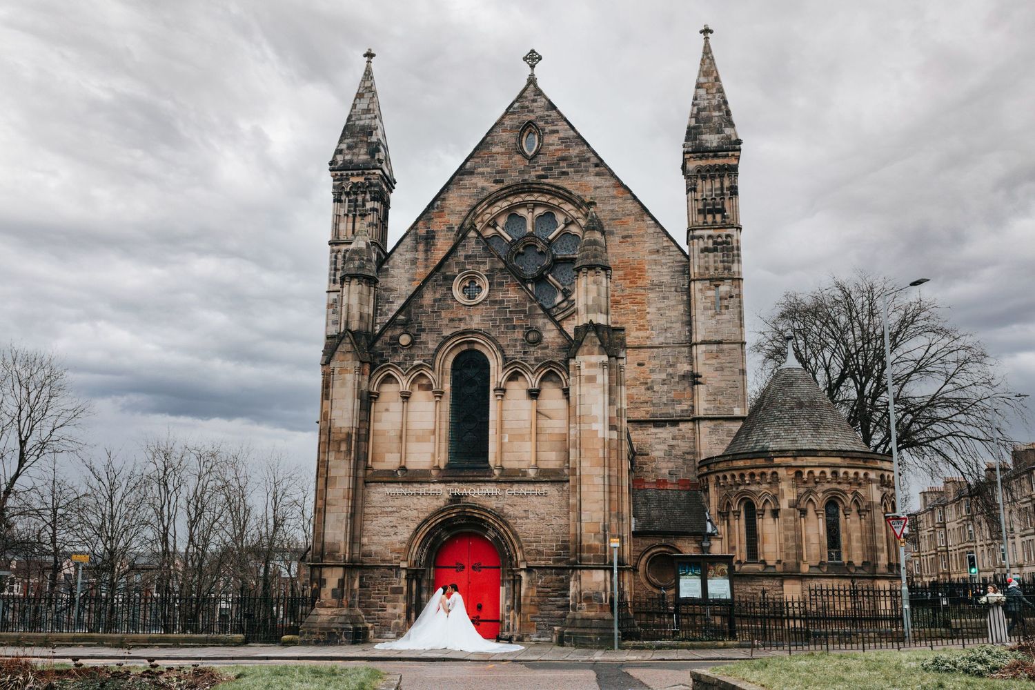 Gothic church exterior with dramatic stone architecture and bright red door on an overcast day in Scotland.