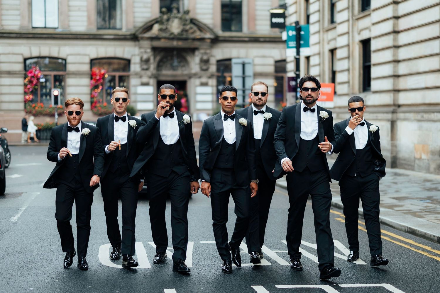 Group of men in black tuxedos and bow ties walking together on a city street.