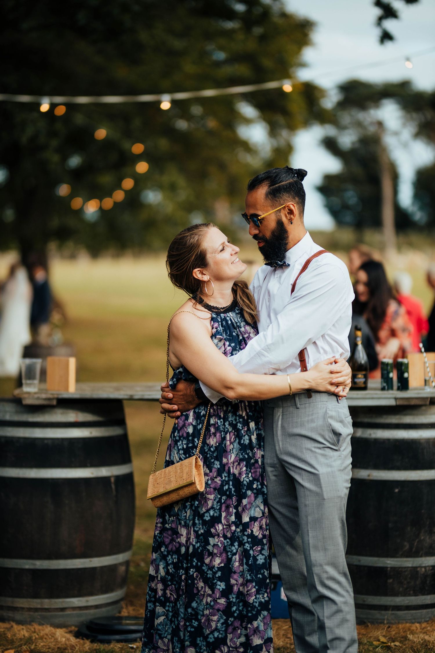 Two people share a romantic dance moment outdoors near wine barrels under string lights at golden hour.