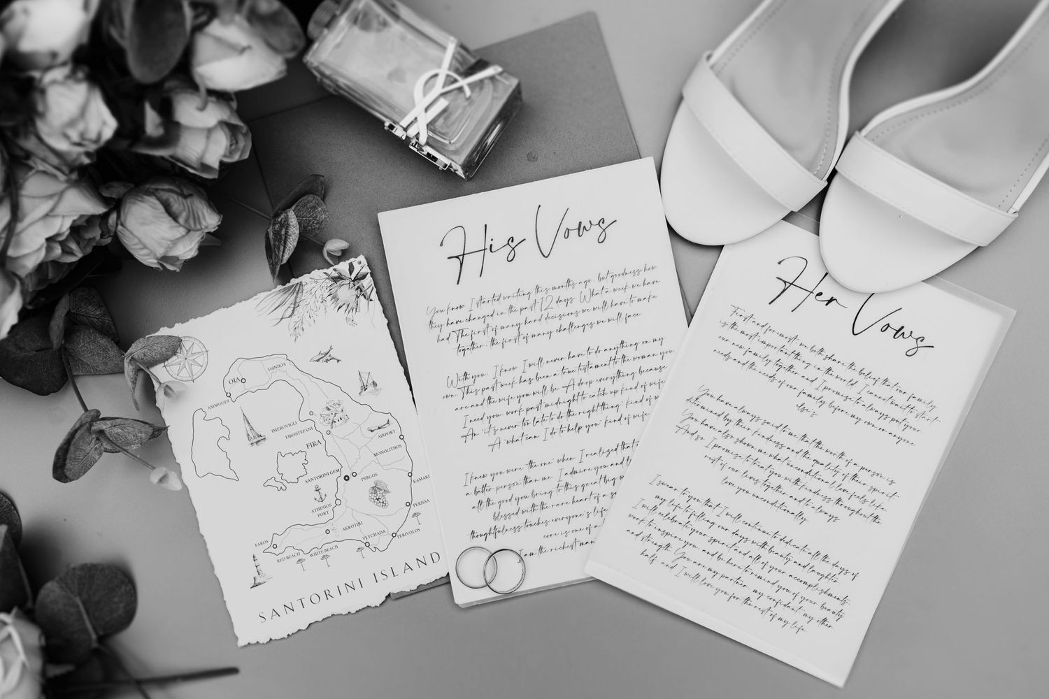 Black and white photograph of handwritten wedding vows with bridal shoes and roses arranged on a gray surface.