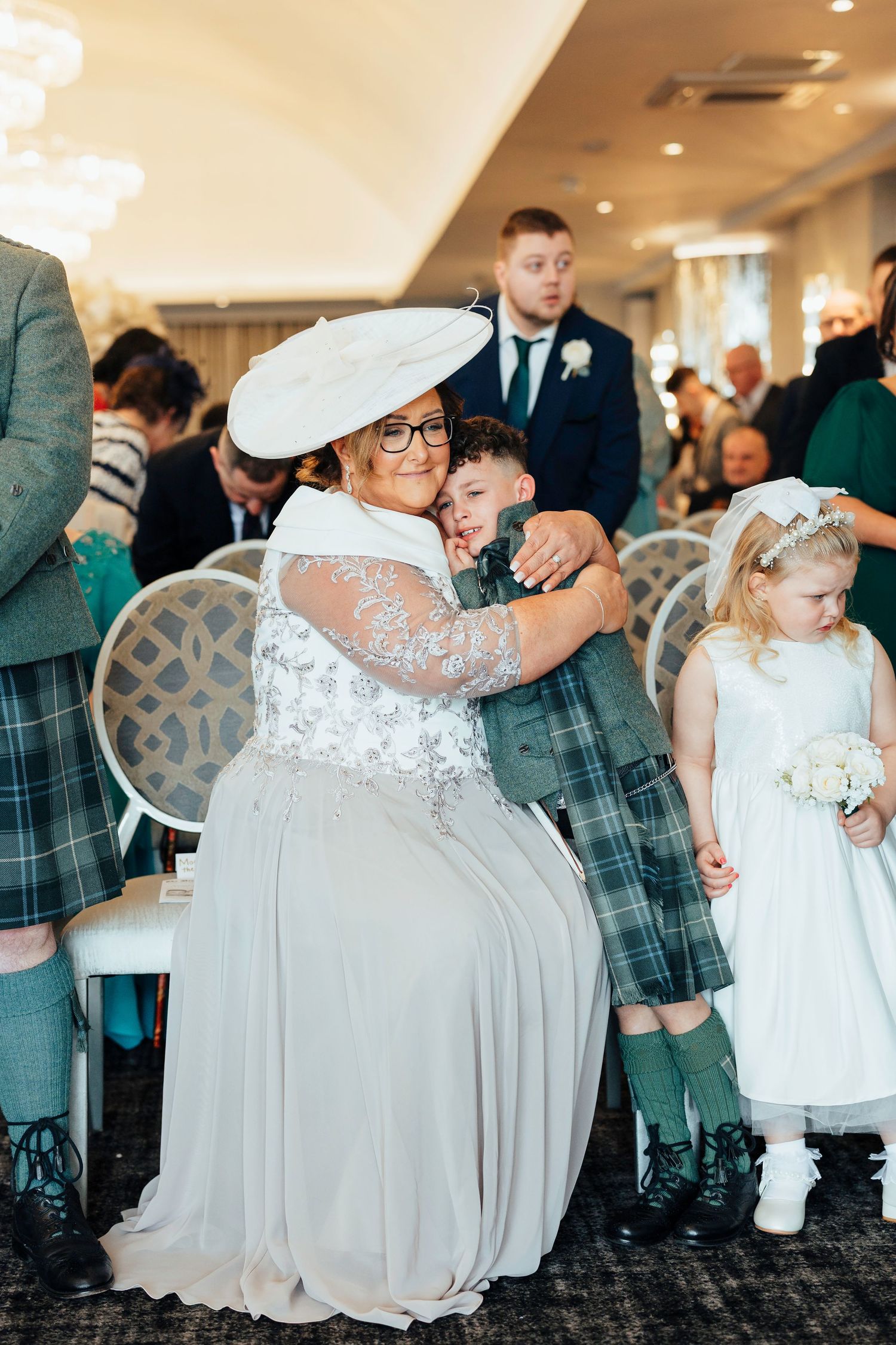 Wedding celebration showing guests in Scottish formal wear including kilts alongside flower girls in white dresses at reception venue.