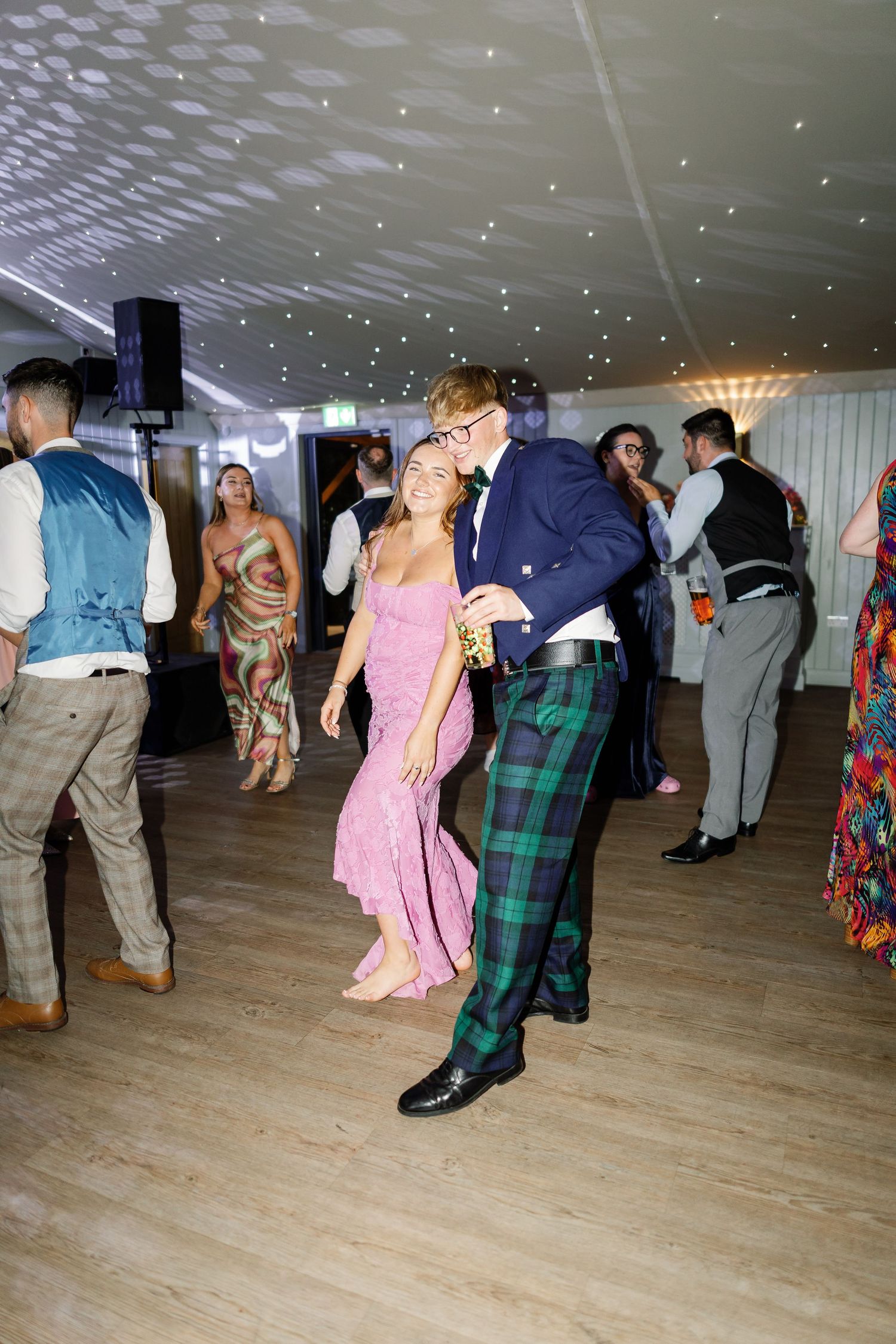 People dancing together on a wooden dance floor under sparkling lights at what appears to be a social gathering or party.