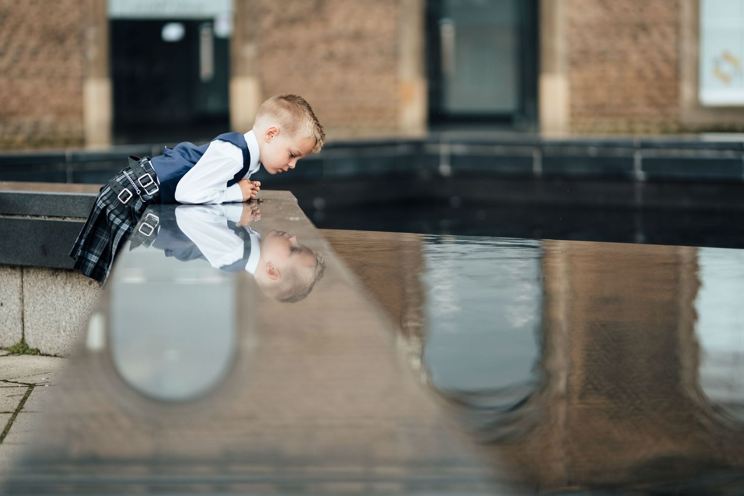 A small child leans over dark reflective marble surface while sitting at a restaurant counter.
