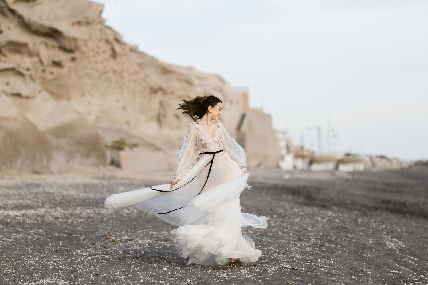 Bride in flowing lace wedding gown twirling on a black sand beach with dramatic cliffs in the background.