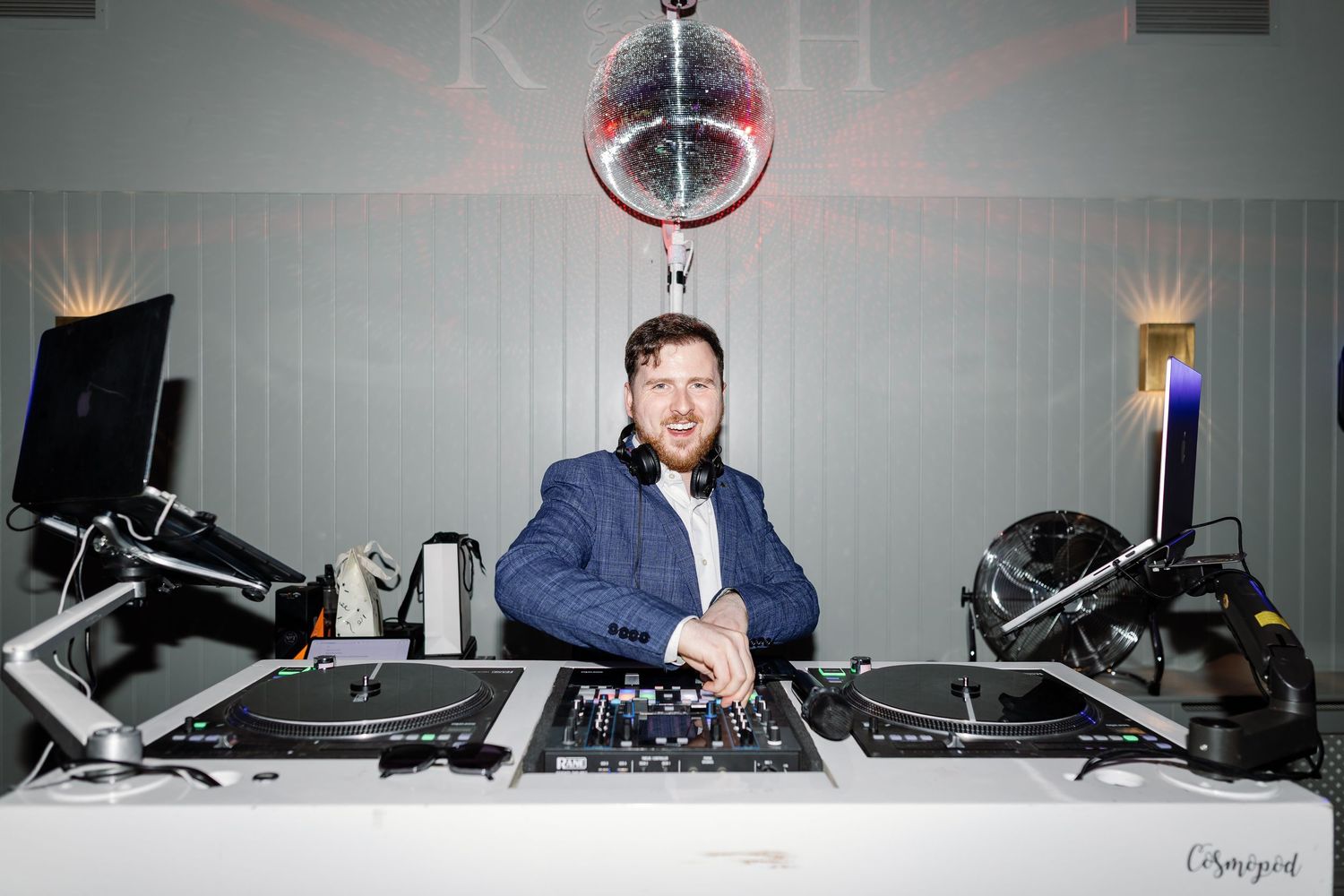 DJ performing at a nightclub behind professional audio equipment and turntables with blue lighting in the background.