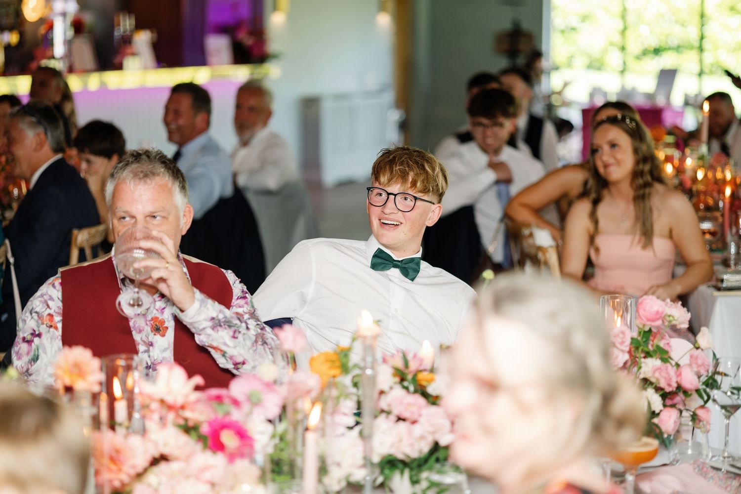 Wedding reception guests seated at long tables with floral centerpieces enjoy dinner and conversation in an elegant venue.