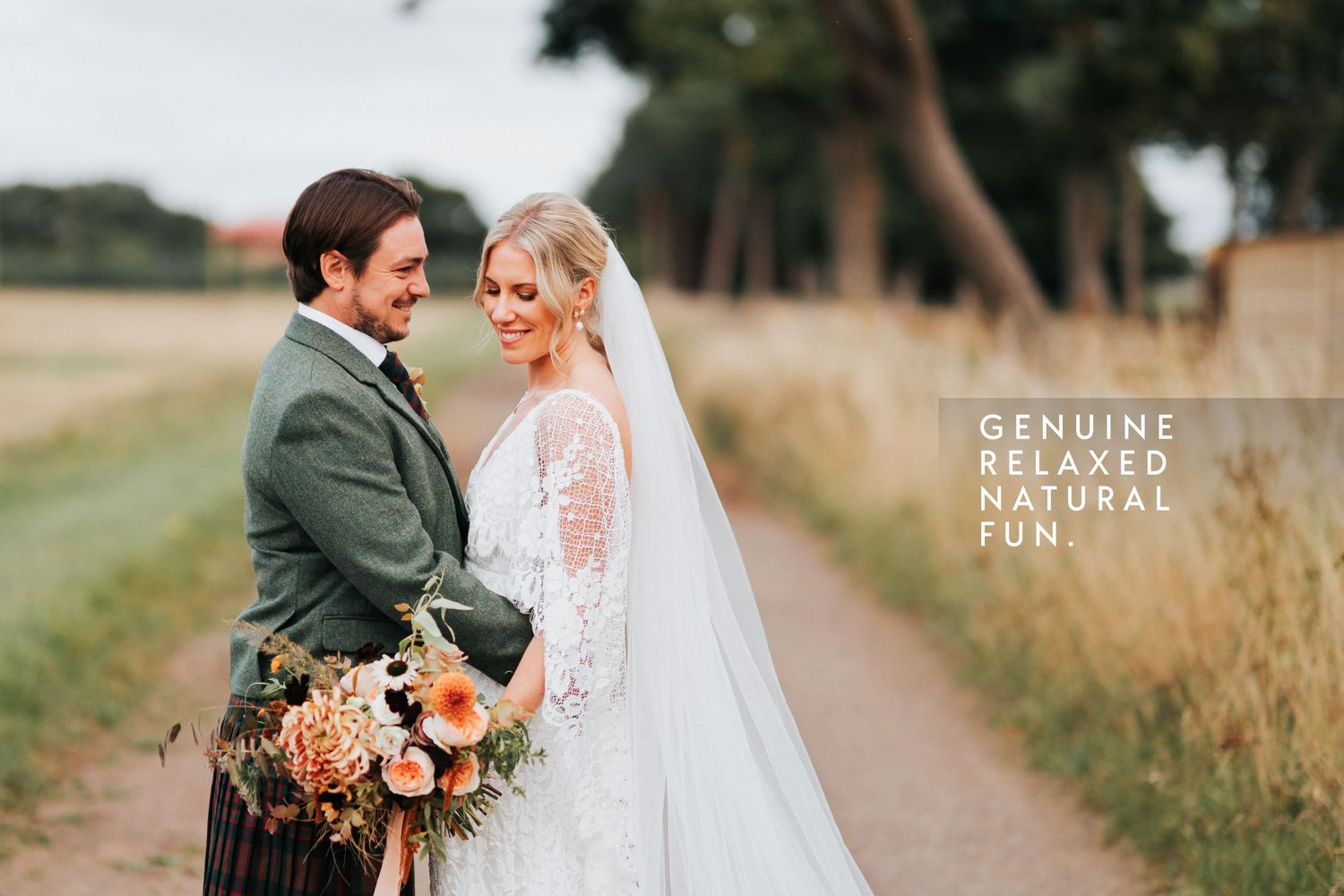 A couple shares a joyful moment on their wedding day in the countryside, with the groom wearing a traditional kilt.