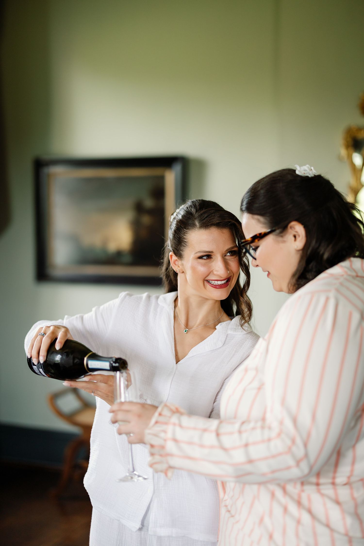 Two people in casual attire share a laugh while pouring drinks together in a dimly lit room.