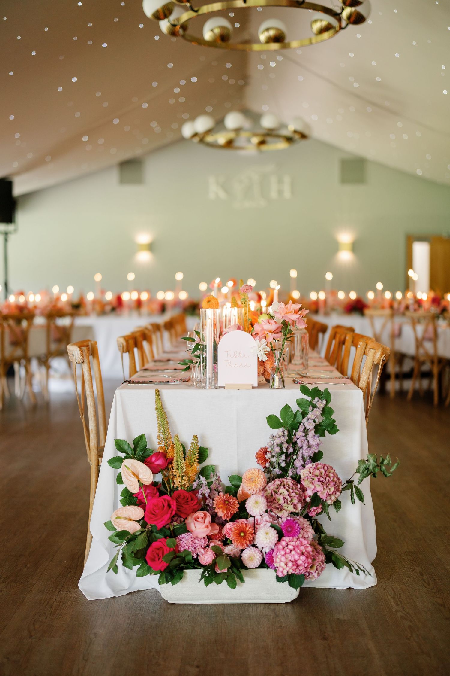 Elegant wedding reception tables decorated with white linens, gold chairs, and lush floral arrangements in pink and red tones.