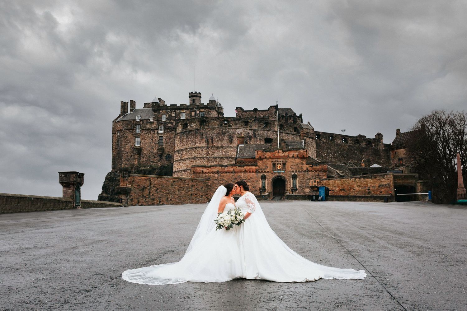 A couple in wedding attire posing in front of the dramatic Edinburgh Castle on a cloudy day.