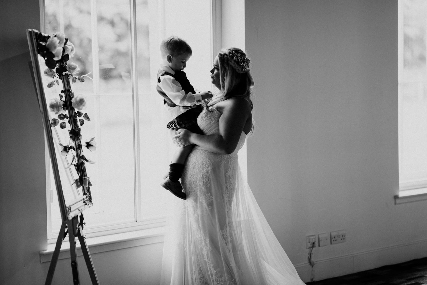 A tender black and white wedding moment next to a window with floral decor.