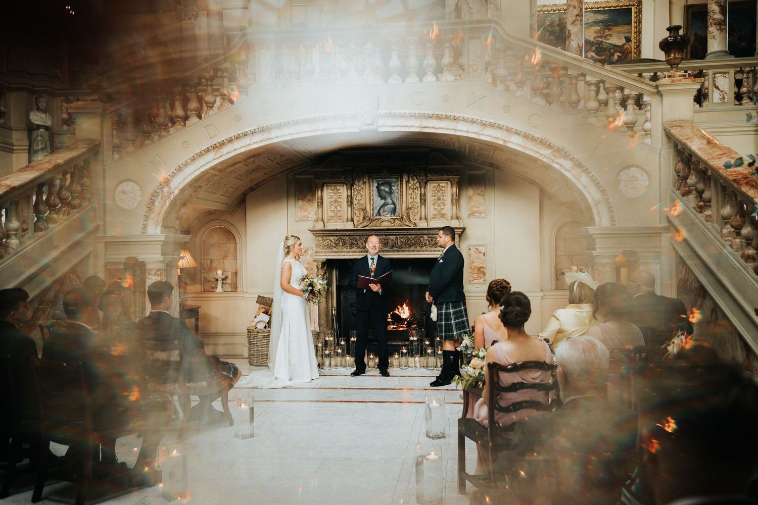 A romantic wedding ceremony takes place under an ornate stone archway in a historic venue with elegant architecture.