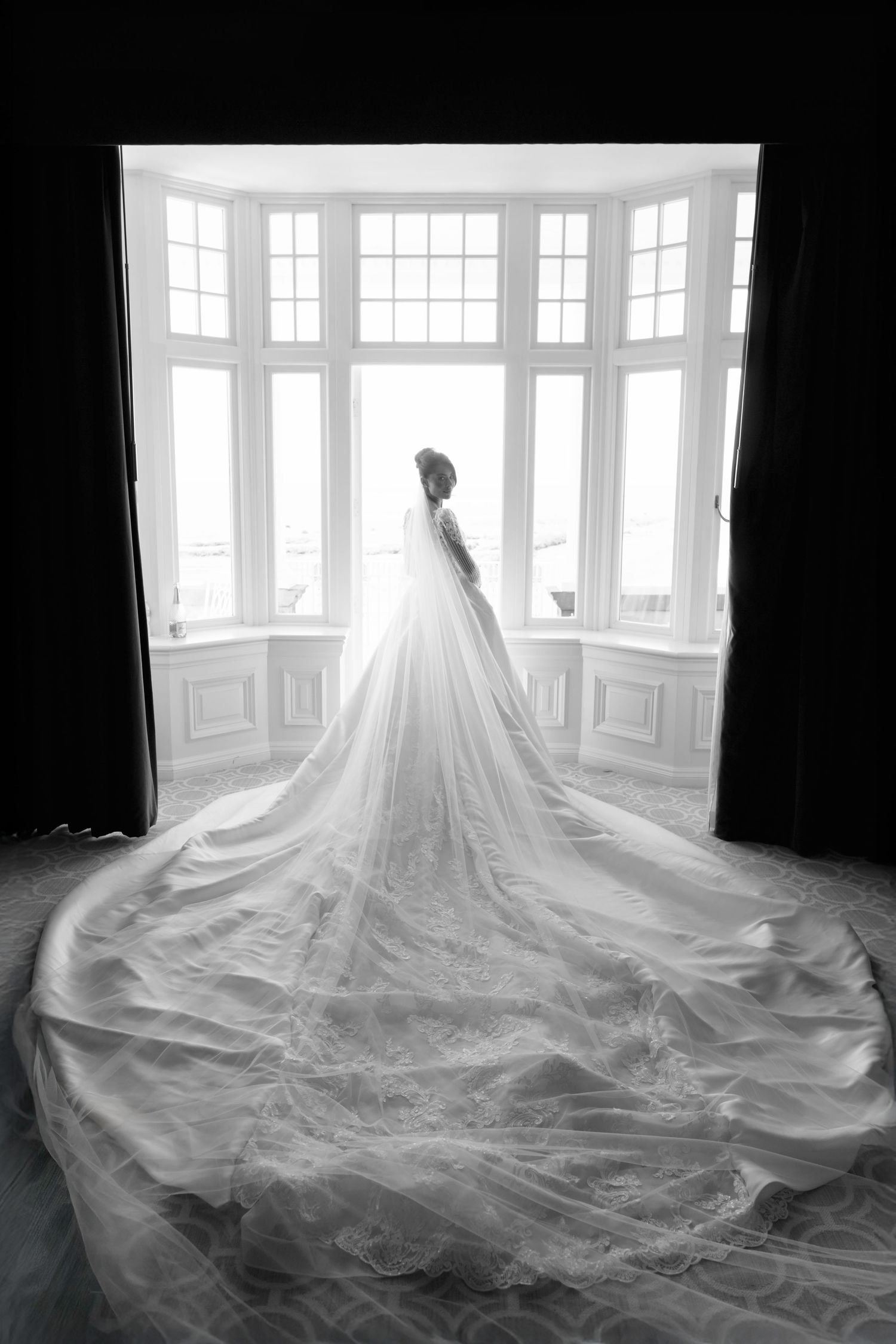 Dramatic black and white bridal portrait showing flowing wedding dress train in bay window in Trump Turnberry Wedding