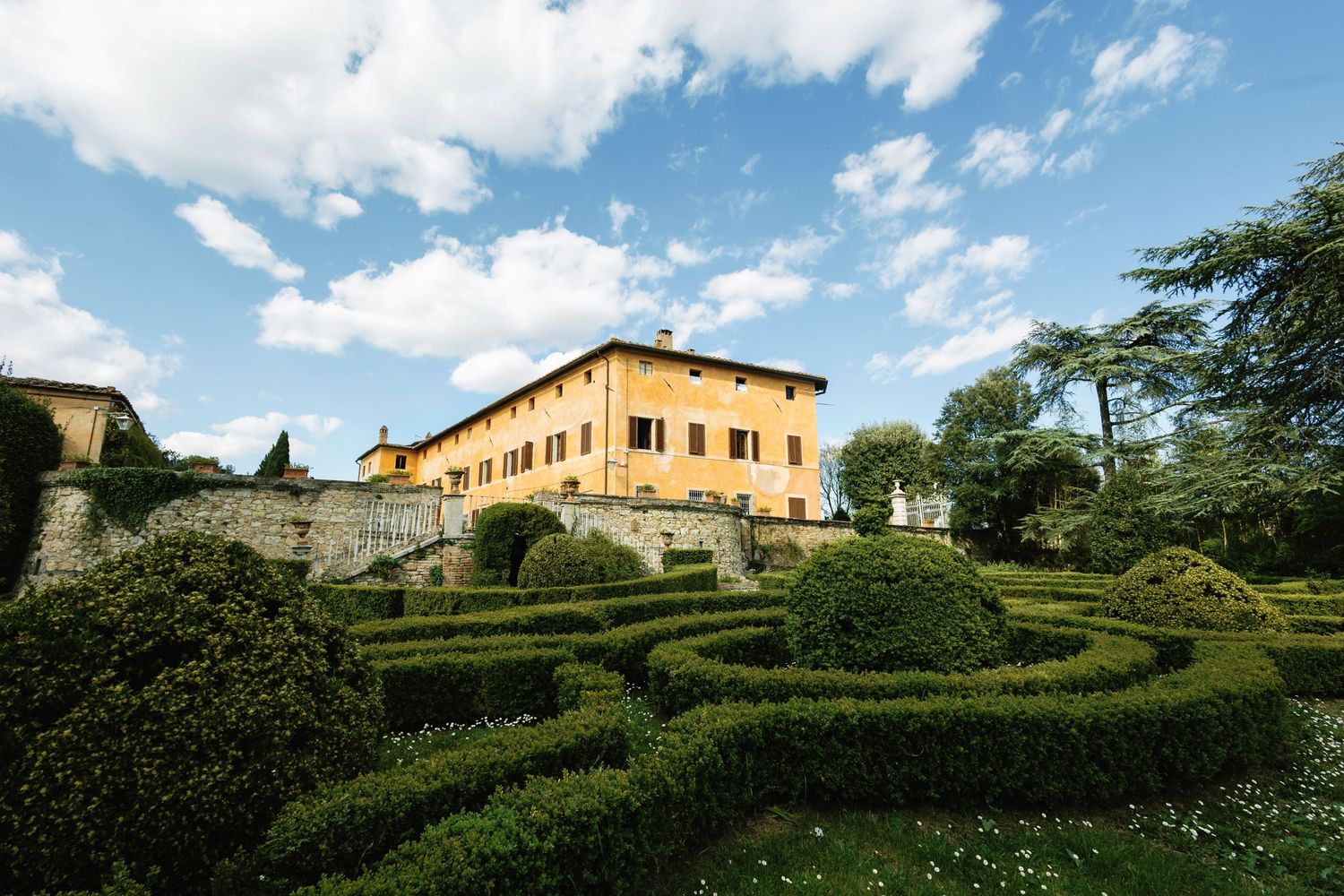Tuscan villa with manicured gardens and hedges under bright blue sky. Villa Catignano Wedding Venue