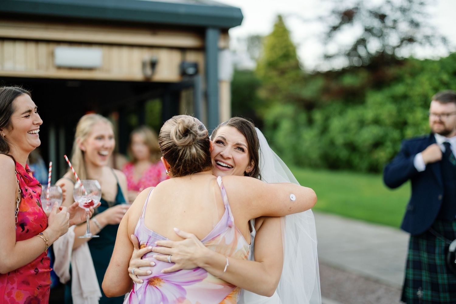 A group of wedding guests react with joy and laughter during an outdoor celebration at a venue.