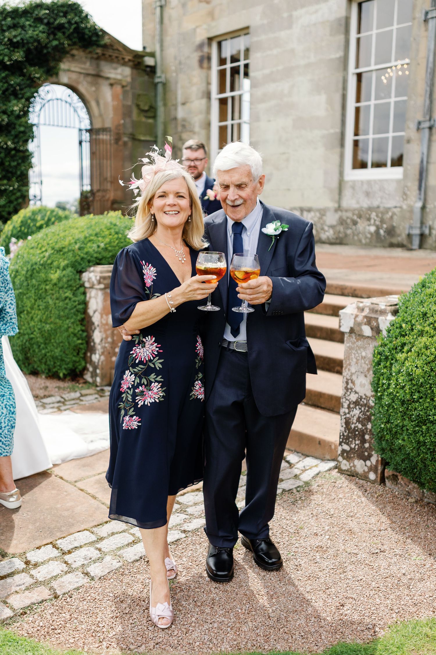 A couple in formal attire toasts with wine glasses on stone steps outside a historic building.