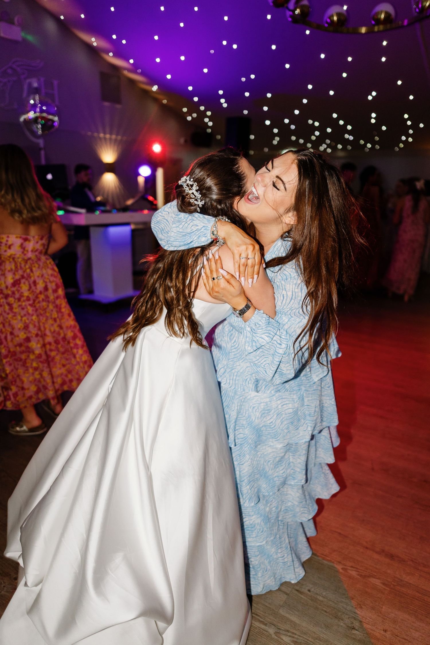 Two people dancing together in a festive venue with purple lighting and twinkling lights overhead.