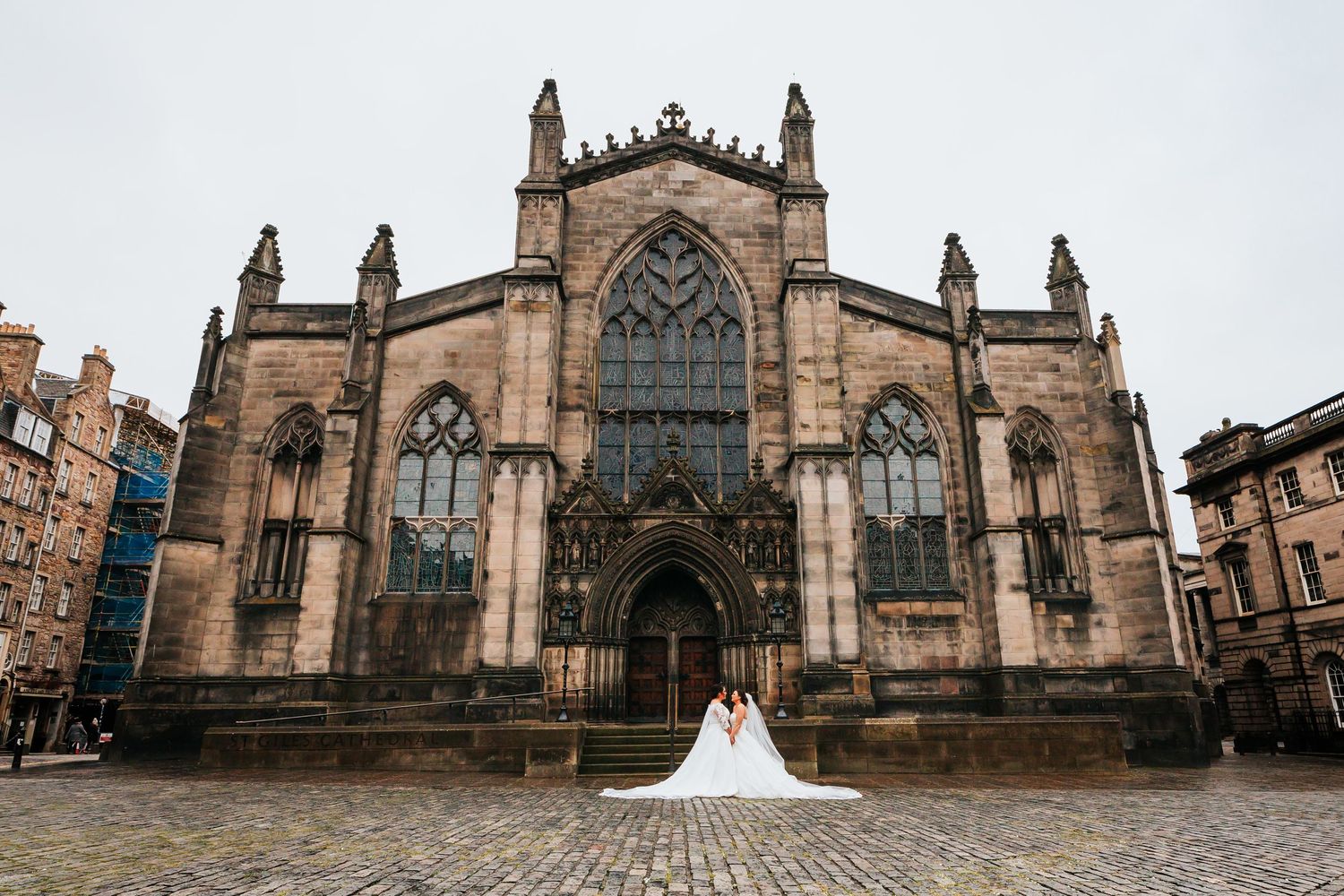 A couple in wedding attire poses in front of the grand gothic St Giles Cathedral in Edinburgh, Scotland on a cloudy day.