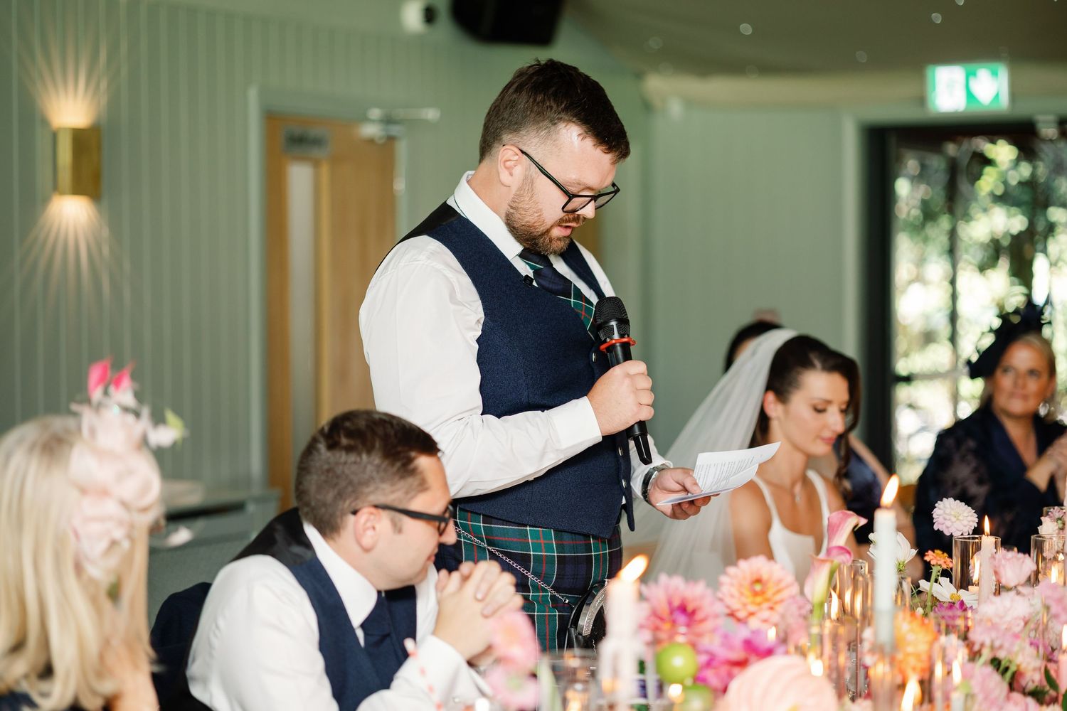 Wedding reception guests enjoy an elegant dinner at long tables decorated with floral centerpieces and glowing candles.