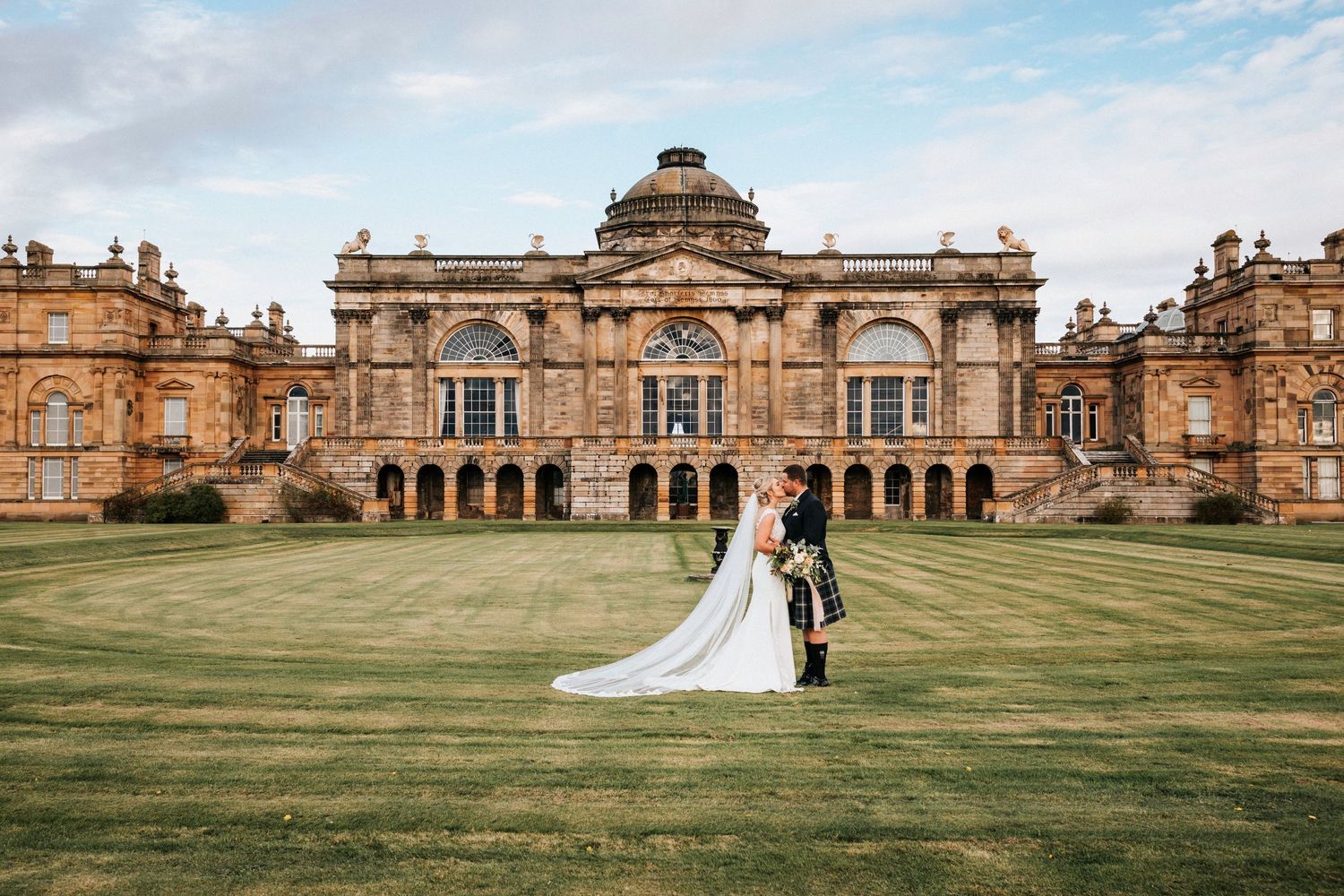 A couple stands on the grand lawn in front of a majestic Victorian mansion at Bowes Museum in County Durham.