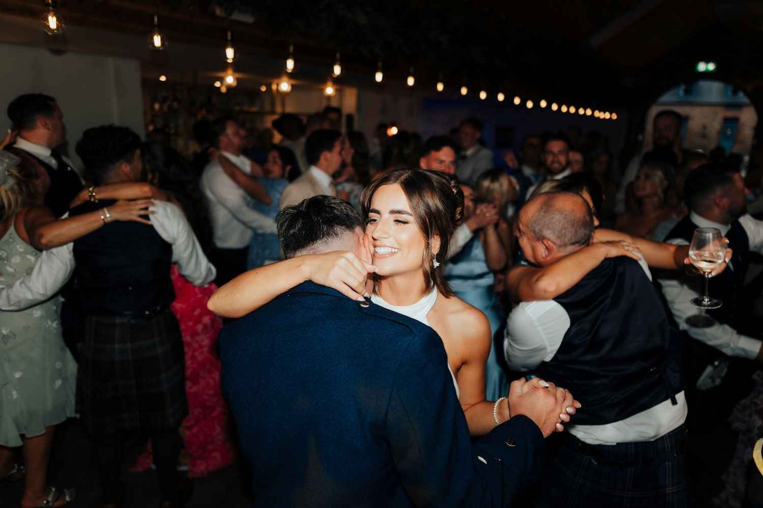 People dancing and socializing at a nighttime event under string lights in a dim venue.