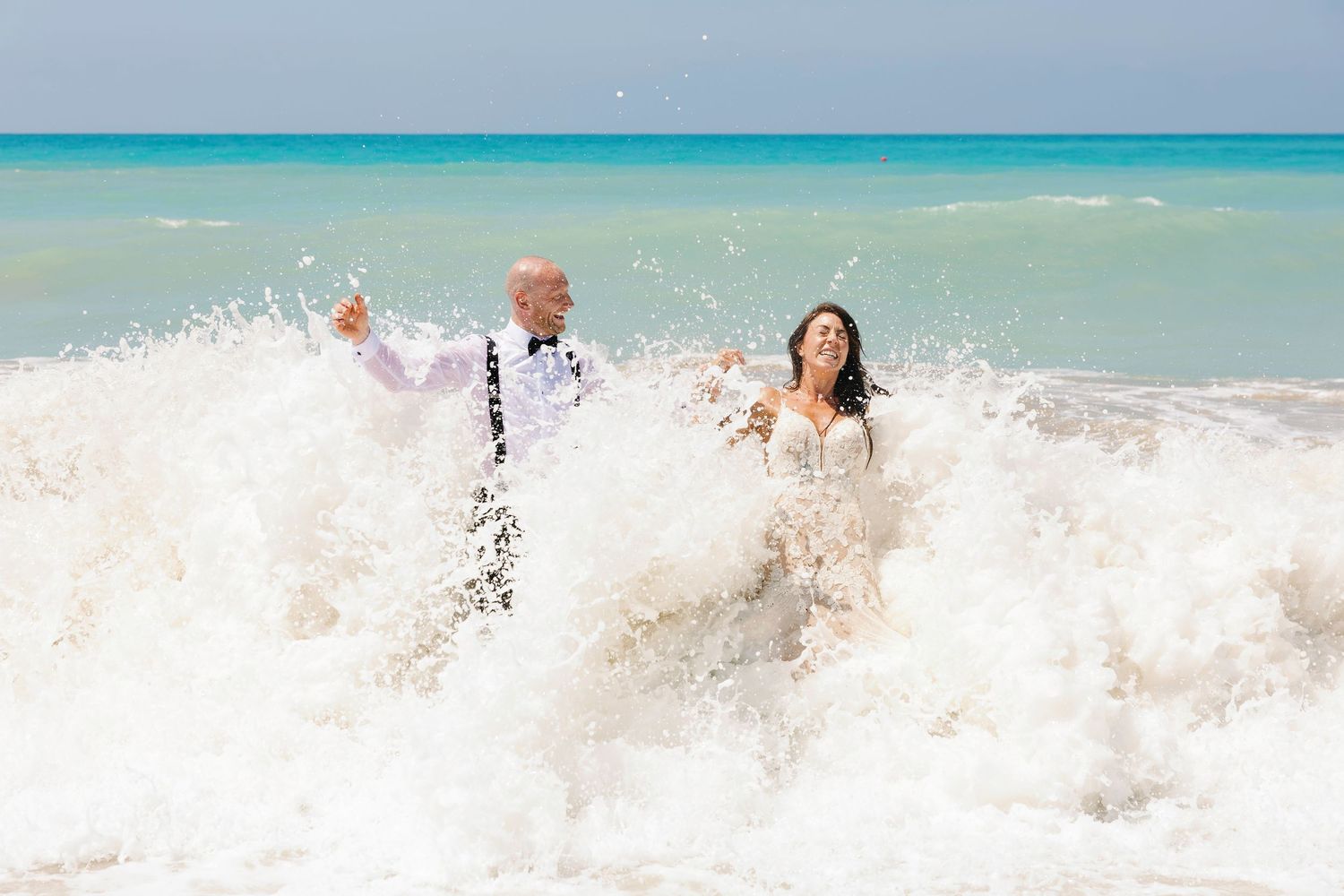 Group splashing and playing in crystal clear turquoise ocean waves at a tropical beach.