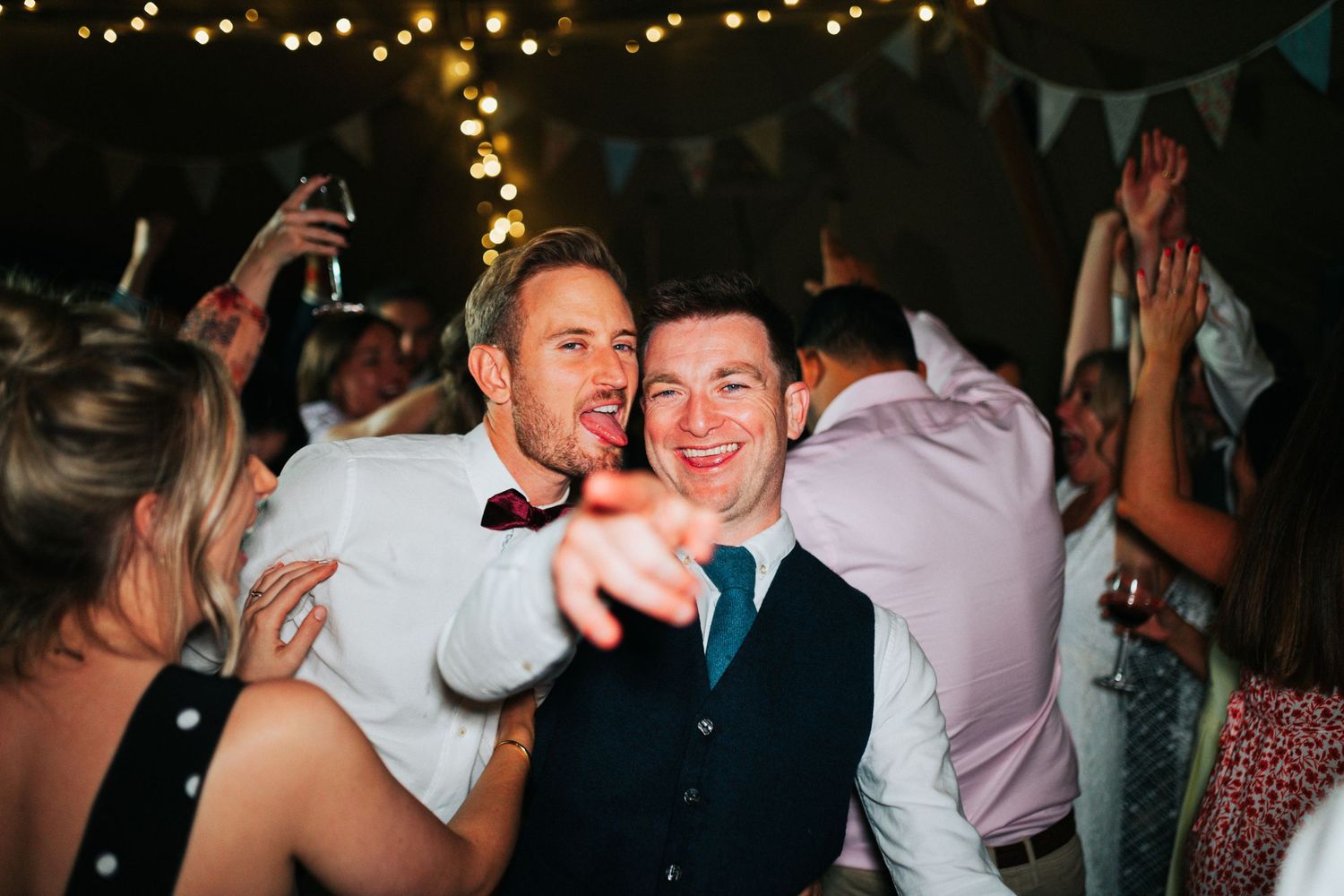People having fun dancing and celebrating at a wedding reception with string lights and bunting decorations.