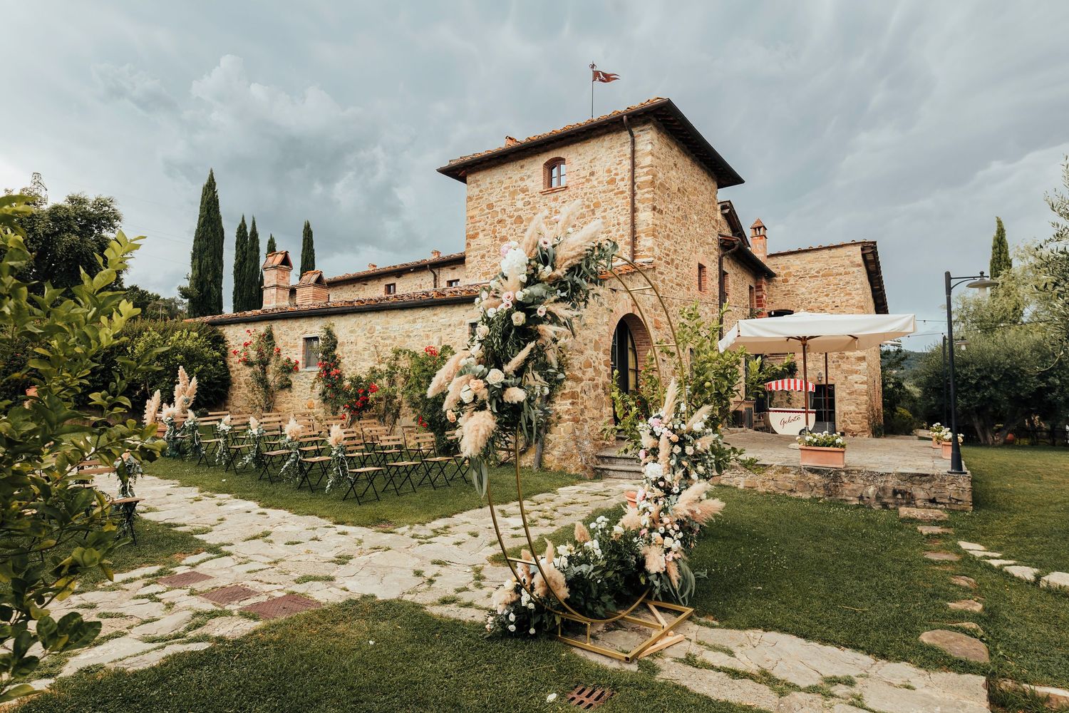 Stone villa with rustic architecture and flowering garden path in Tuscany on a cloudy day.