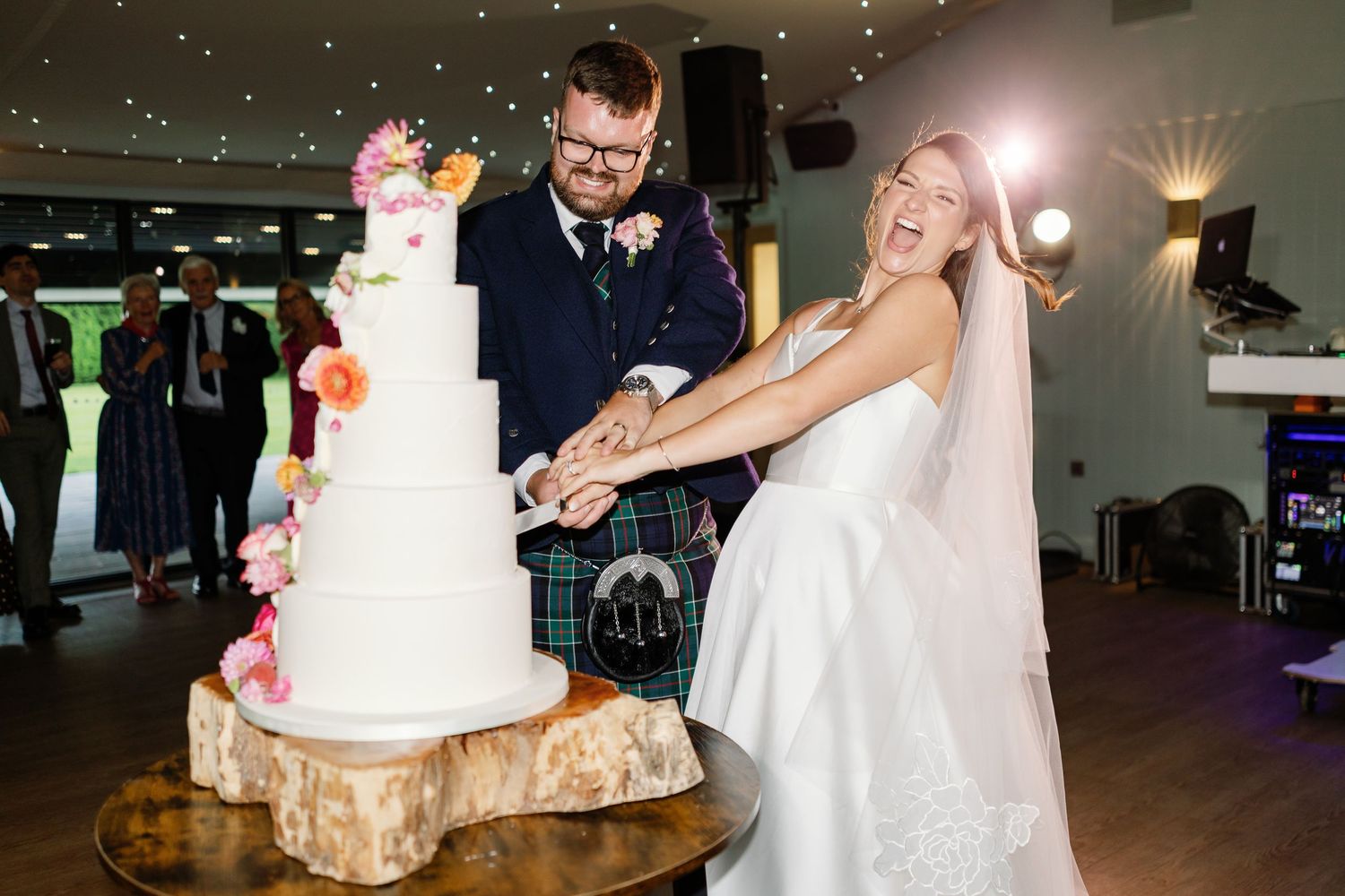 Wedding couple cuts their elegant white tiered cake during reception celebration.