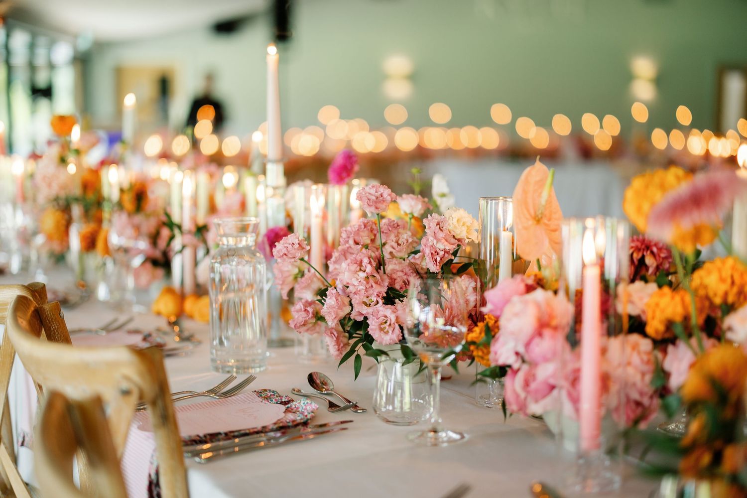 Elegant wedding reception table decorated with pink and orange floral arrangements and glowing candles in a romantic setting.