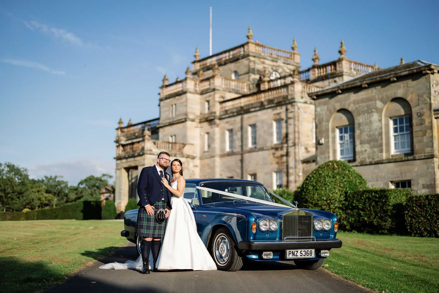 “Bride and groom standing in front of Kinmount House, a stately Scottish mansion with sweeping lawns and classic architecture.”