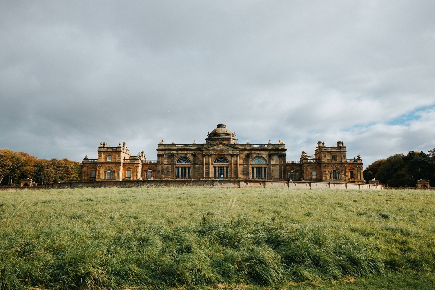 Historic Seaton Delaval Hall stands majestically across a green field under moody skies in Northumberland, England.