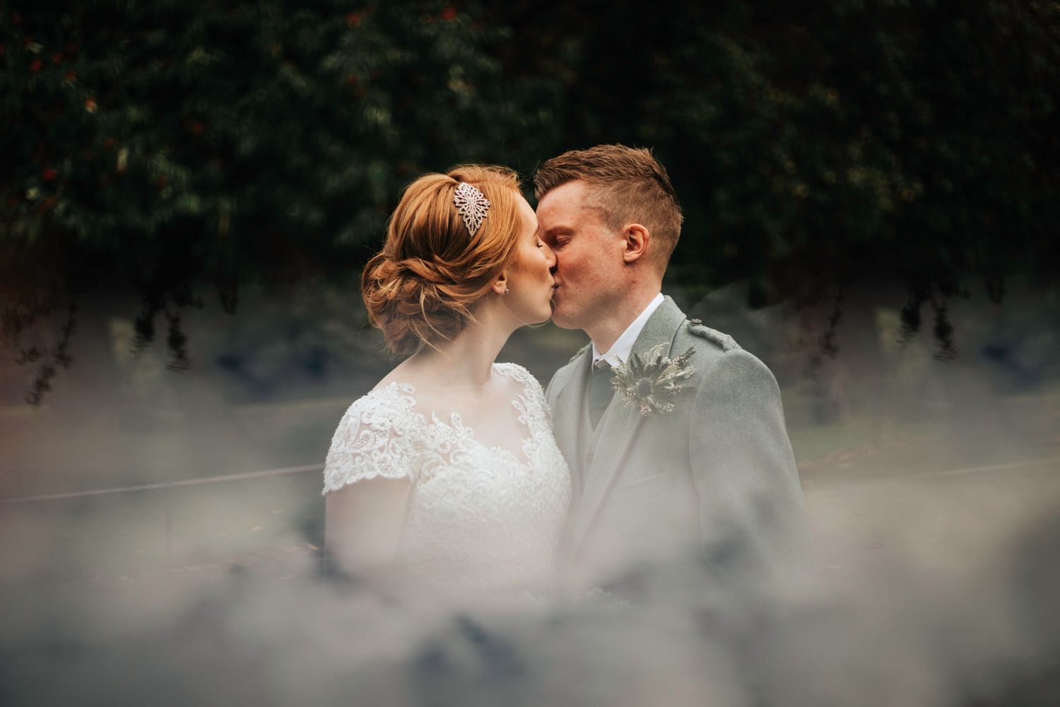 A romantic wedding photo of a couple sharing an intimate moment surrounded by soft misty foliage.