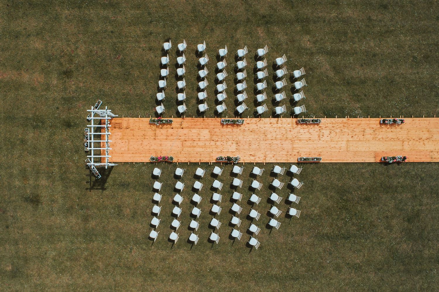 Aerial view of white chairs arranged symmetrically on a green lawn with a wooden boardwalk across the middle.