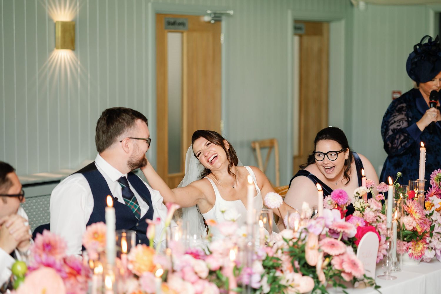 A long banquet table decorated with pink floral centerpieces and glowing candles for an elegant wedding reception.