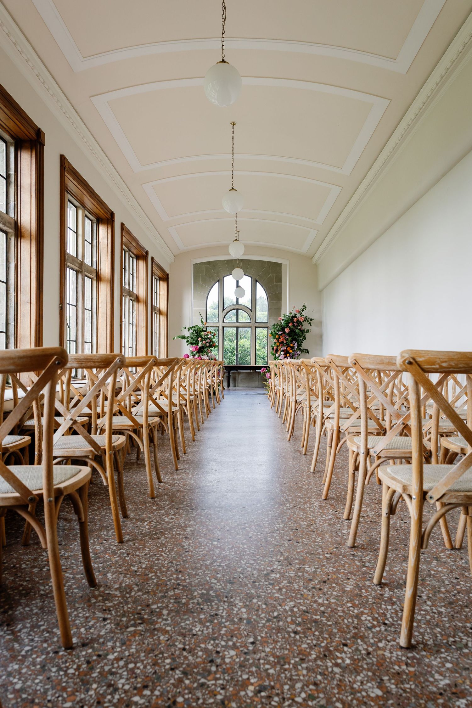 Long corridor with white vaulted ceiling and rows of wooden chairs along both sides creating symmetrical perspective.