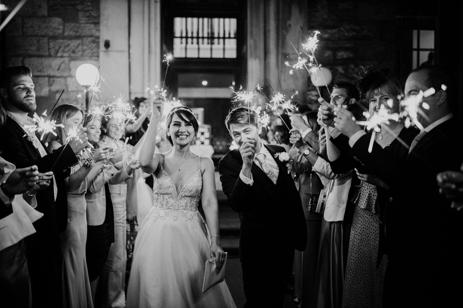 Wedding guests celebrate with sparklers at night during a joyful black and white reception exit.
