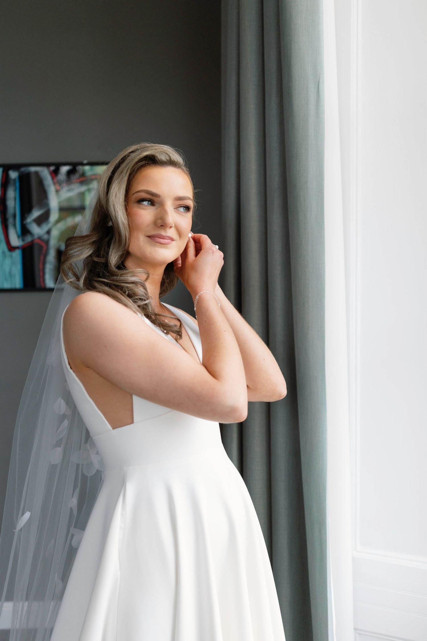 Bride in classic white dress with veil poses by window in modern setting Carlowrie Castle