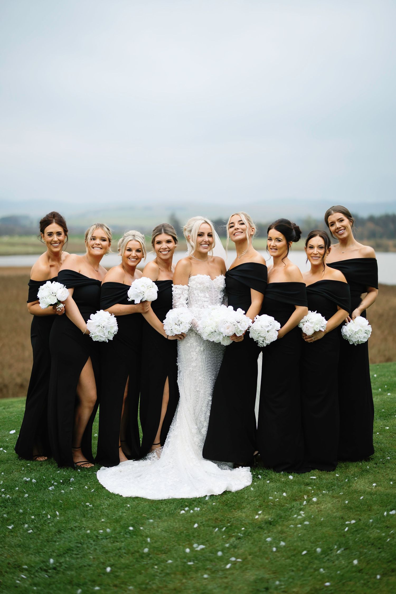 Wedding party in black dresses and white gown pose playfully in a series of creative group photos on grassy field.