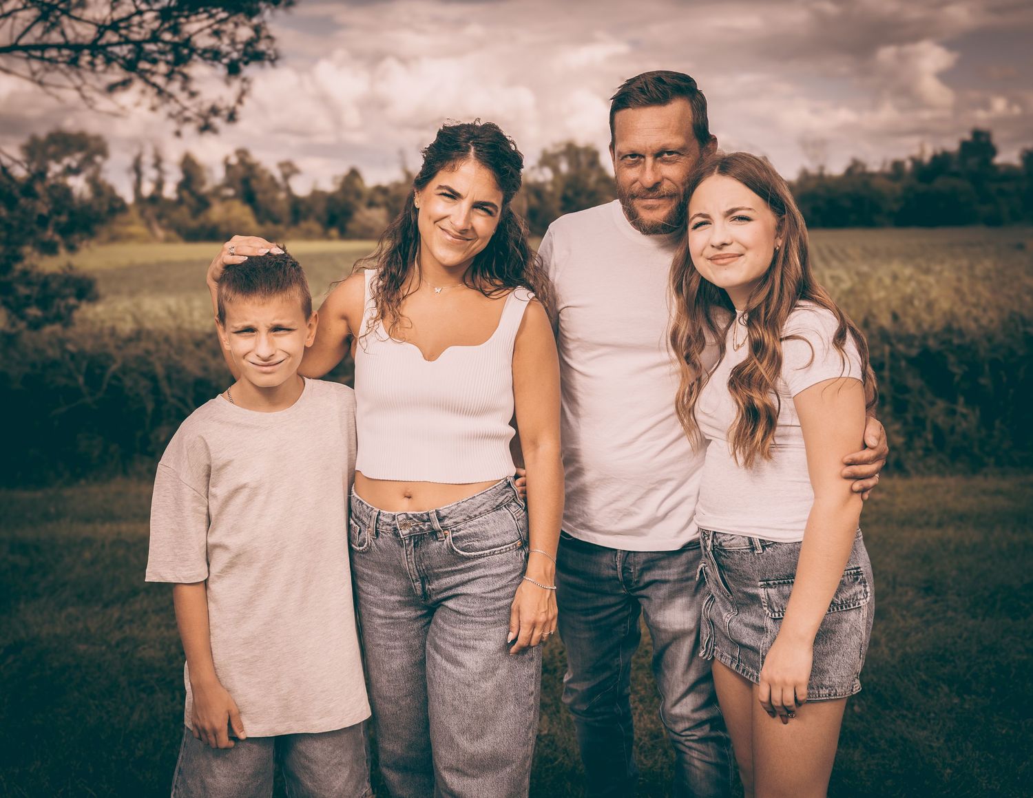 Casual family portrait of four people standing together in an outdoor field.