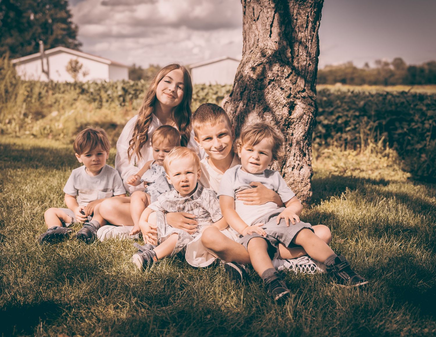 A warm vintage-toned family portrait of parents and young children sitting together under a tree.
