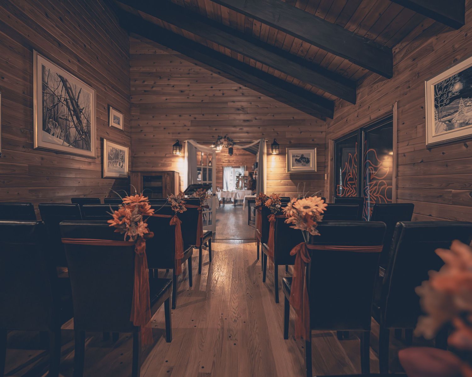 Rustic wooden chapel interior with dark pews, orange floral arrangements and warm lighting along the aisle.