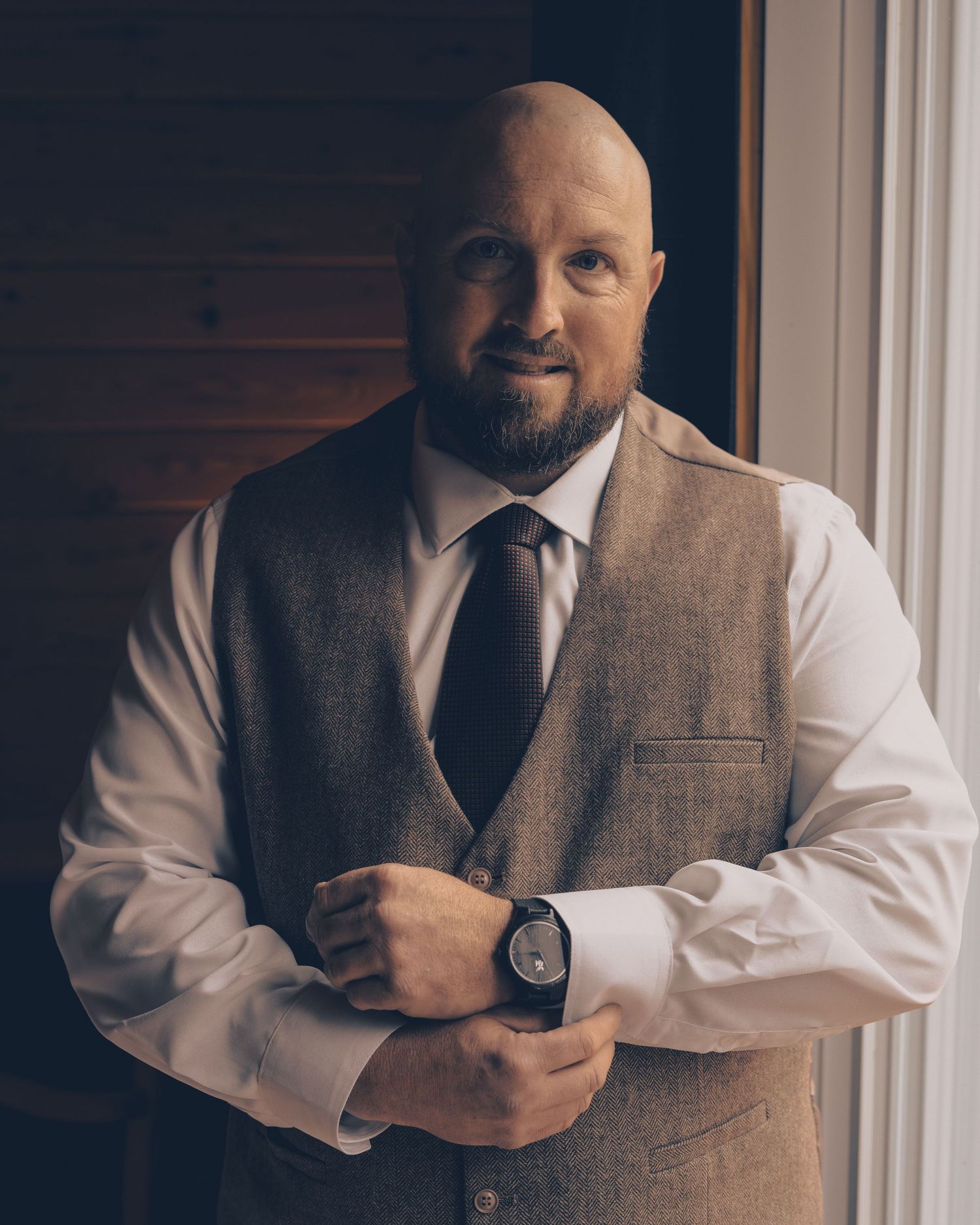 A formal portrait of a person wearing a brown vest and white dress shirt in natural window light.