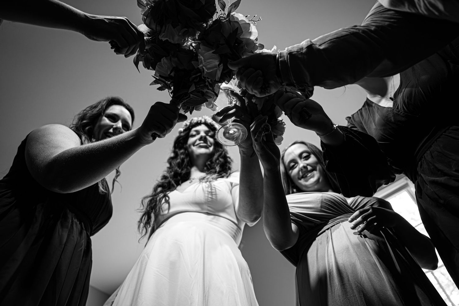 Black and white photo of wedding party joining hands in a circle overhead.