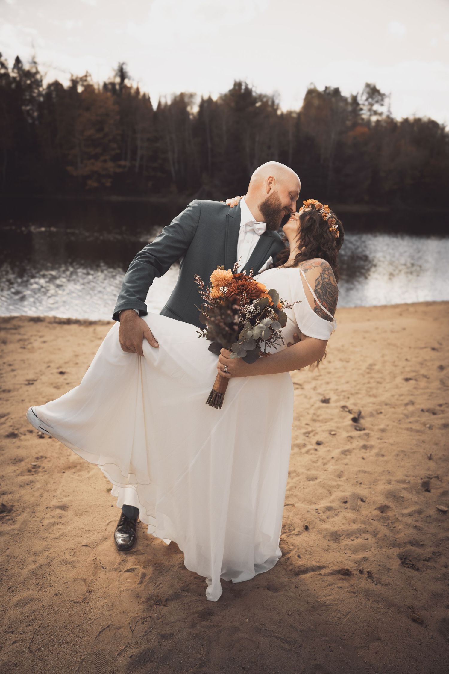 A romantic wedding moment on a beach with fall foliage in the background.