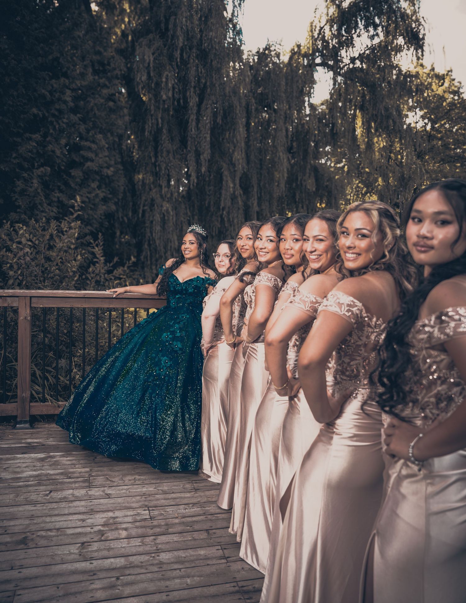 Bridal party lineup with teal gown and champagne bridesmaid dresses on wooden deck.